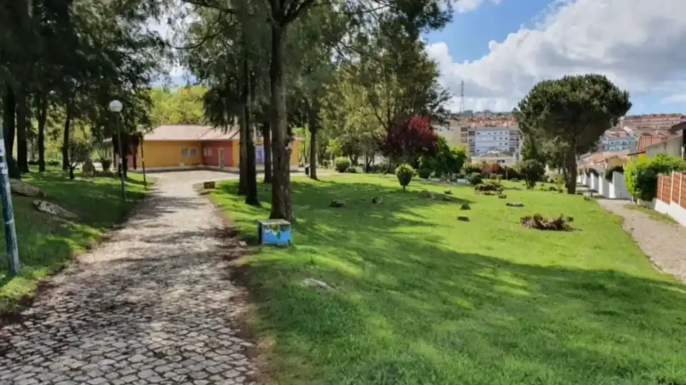 Jardim da Anta, em Agualva: caminho de calçada entre relva e árvores, num dia de sol.
